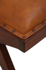 Cadenza Bench With Inverted Base. Tan leather bench. Teak wood base. Inverted V legs. Genuine leather upholstery. Nail head trim. Rustic modern bench. Luxury accent seating. Handcrafted furniture. Vintage-inspired design.