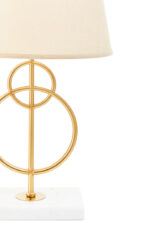 Raya Gold Circles Table Lamp. Gold table lamp. White marble base lamp. Beige linen shade lamp. Art deco lighting. Modern gold lamp. Luxury table light. Elegant bedside lamp. Contemporary lighting design. Sculptural metal lamp. Living room lighting. Bedroom table lamp. Marble and gold décor. Boutique home accessory. Ambient light fixture. Minimalist table lamp. Designer home lighting. Statement lamp design. Modern art deco décor.