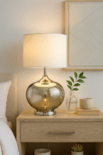 Perrin Ball Shaped Table Lamp. Glass base lamp. Metallic finish lamp. Chrome table lamp. Modern bedside lighting. Contemporary home décor. Elegant living room lamp. White fabric shade. Minimalist glass lighting. Designer accent lamp. Reflective glass lamp. Soft ambient light. Boutique style lamp. Classic meets modern lighting.