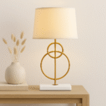 Raya Gold Circles Table Lamp. Gold table lamp. White marble base lamp. Beige linen shade lamp. Art deco lighting. Modern gold lamp. Luxury table light. Elegant bedside lamp. Contemporary lighting design. Sculptural metal lamp. Living room lighting. Bedroom table lamp. Marble and gold décor. Boutique home accessory. Ambient light fixture. Minimalist table lamp. Designer home lighting. Statement lamp design. Modern art deco décor.