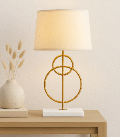 Raya Gold Circles Table Lamp. Gold table lamp. White marble base lamp. Beige linen shade lamp. Art deco lighting. Modern gold lamp. Luxury table light. Elegant bedside lamp. Contemporary lighting design. Sculptural metal lamp. Living room lighting. Bedroom table lamp. Marble and gold décor. Boutique home accessory. Ambient light fixture. Minimalist table lamp. Designer home lighting. Statement lamp design. Modern art deco décor.